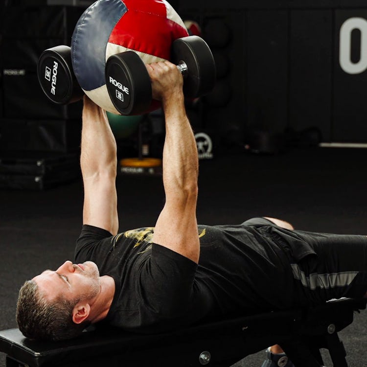 Man performs dumbbell hex press with medicine ball